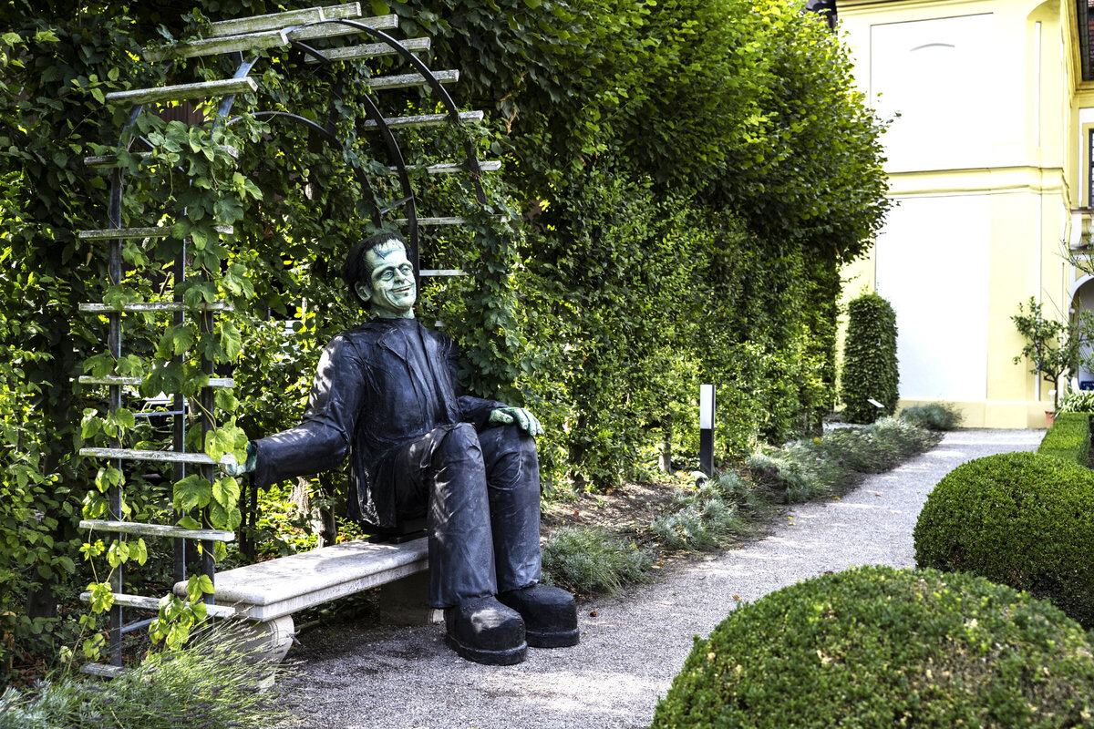 Im Anatomiegarten wartet die Kreatur auf einer Gartenbank auf Besucherinnen und Besucher. 