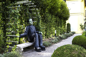 Bild vergr&ouml;&szlig;ern: Im Anatomiegarten wartet die Kreatur auf einer Gartenbank auf Besucherinnen und Besucher.